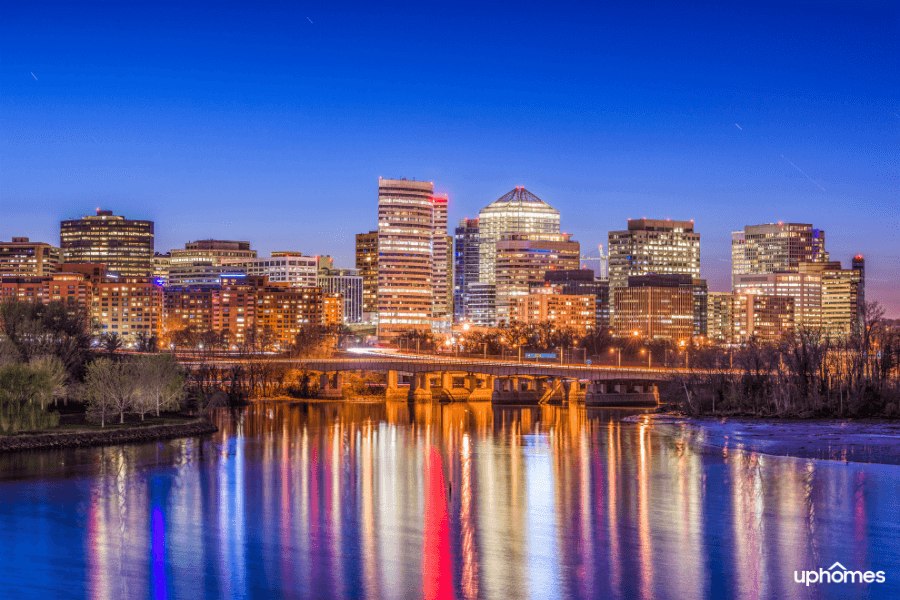 A photo of Arlington Virginia at night time with water reflecting the colorful city lights