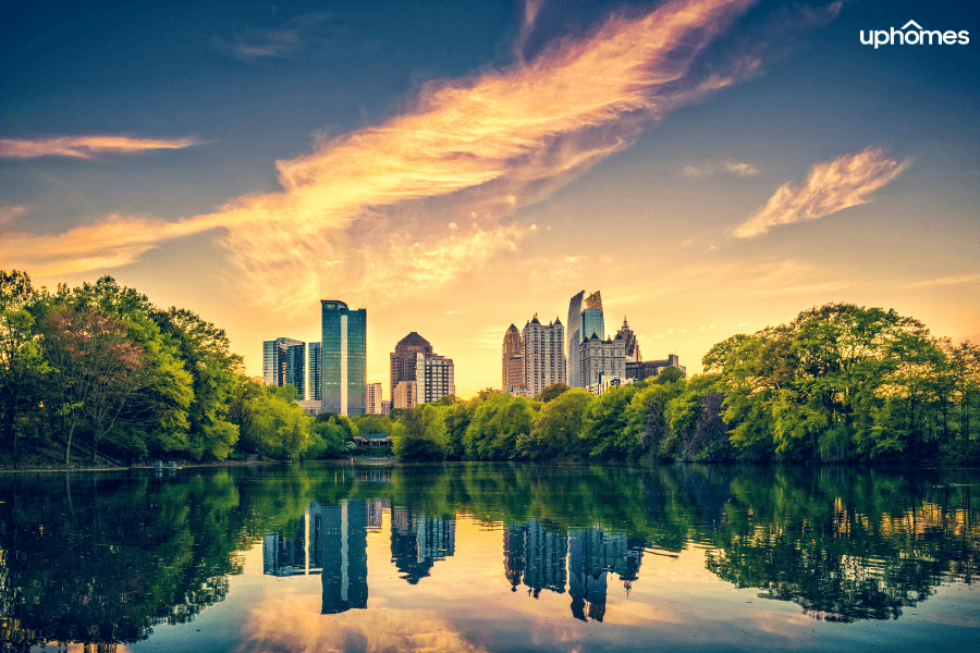 A photo of Atlanta, Georgia with the sun setting over the skyline of downtown in the background and a pond in the foreground with leaves beginning to change color in the fall