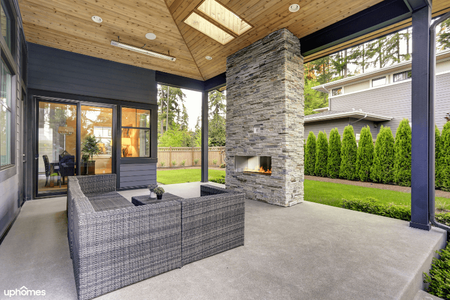 A backyard patio with a stone fireplace and an overhang that allows protection from inclement weather