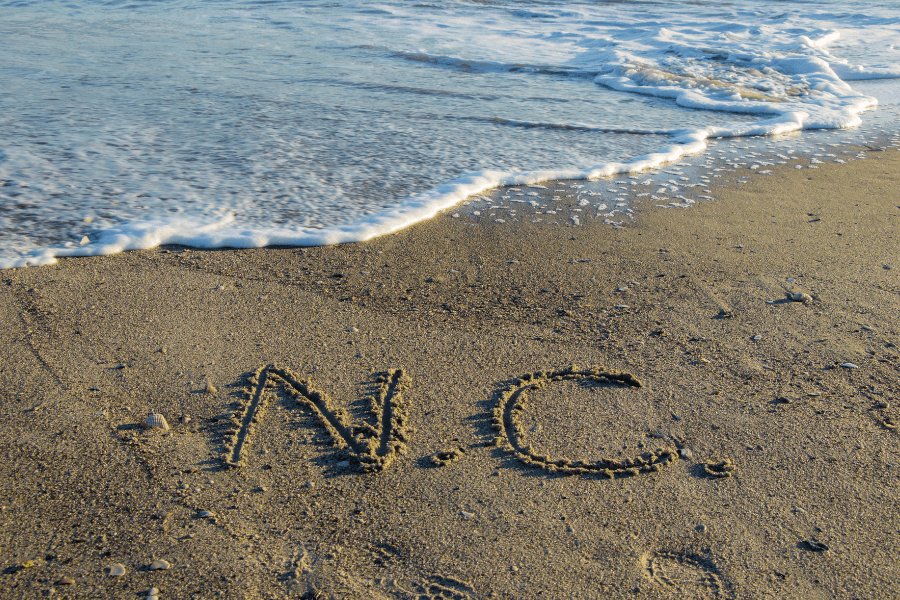 NC written in the sand at a North Carolina beach as the tide rolls in