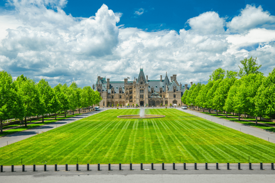The Biltmore Estate in Asheville North Carolina with beautiful green grass, trees, blue sky with clouds and the Biltmore castle