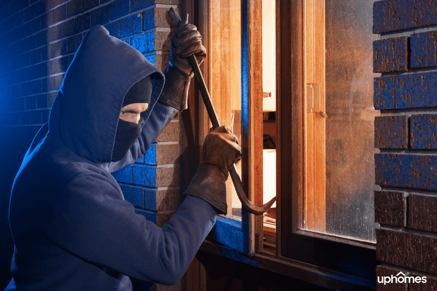 A burglary taking place as a thief uses a crowbar to sneak in a window of a home that is on the ground level