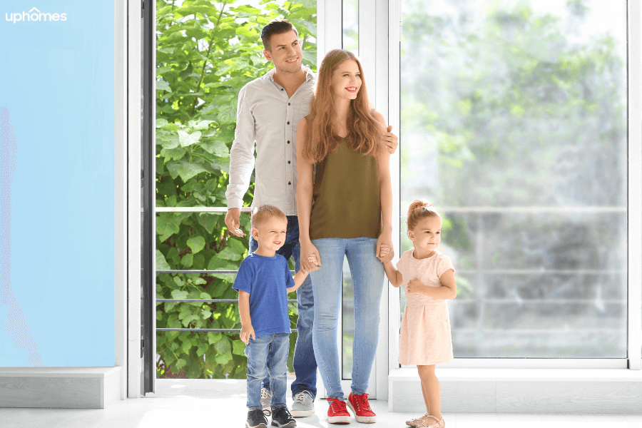 Family moving into a new home with the baby boy and girl holding mom's hands while the dad smiles watching