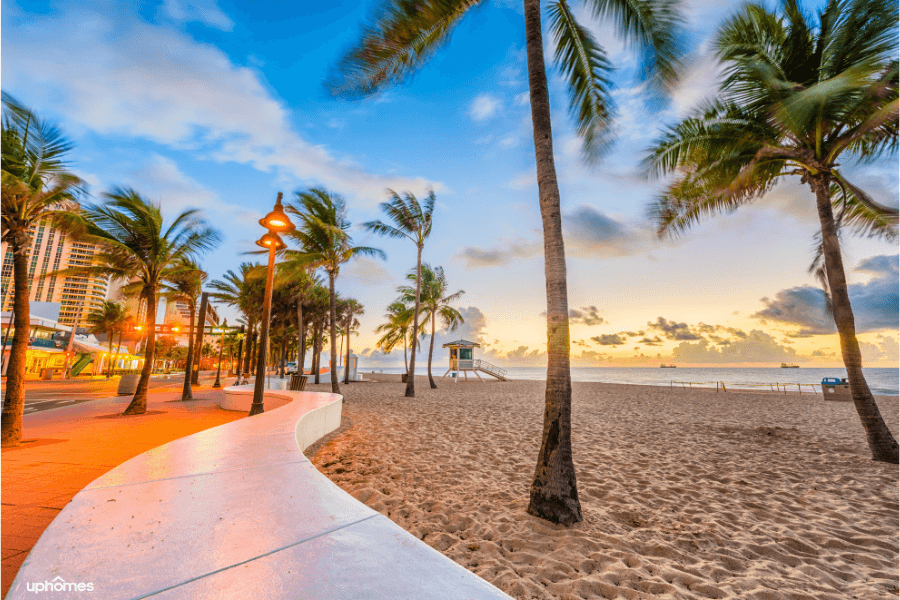 Fort Myers beach and boardwalk with a picture of the beach, sand, palm trees, and city buildings at sunset