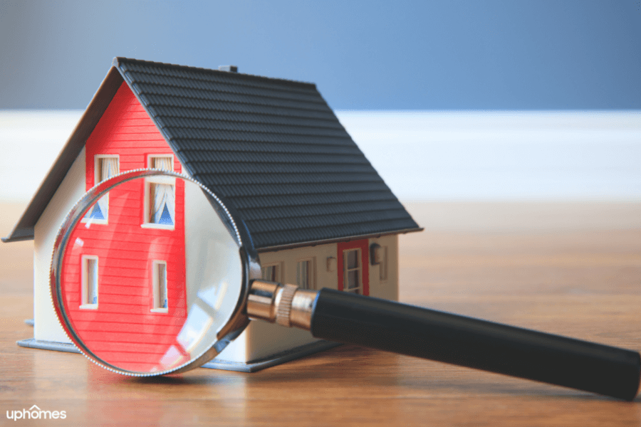 A magnifying glass in front of a toy home that symbolizes a home search