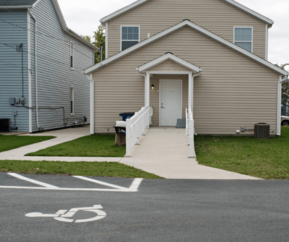 View of the rear entrance to a home with a wheelchair-accessible ramp leading up to the door, and a handicap parking sign painted on the asphalt.