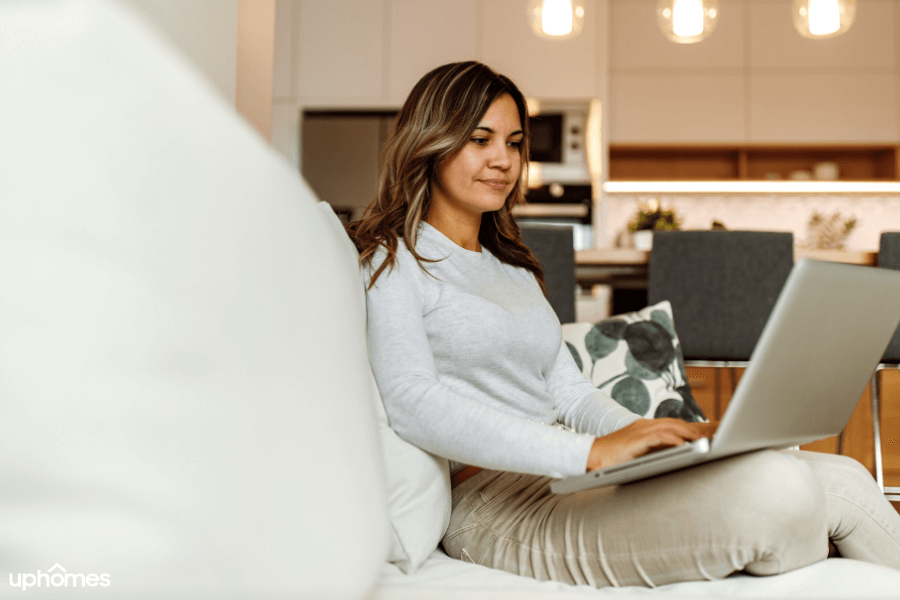 A woman who is living alone sitting on the couch working on her laptop 
