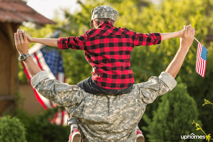 Military father with son on his shoulders and american flag with the sun shining in the background