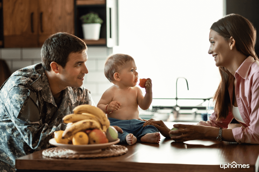 Military family with son inside the home in the kitchen with baby boy eating an apple while dad is in uniform and mom is happy and smiling