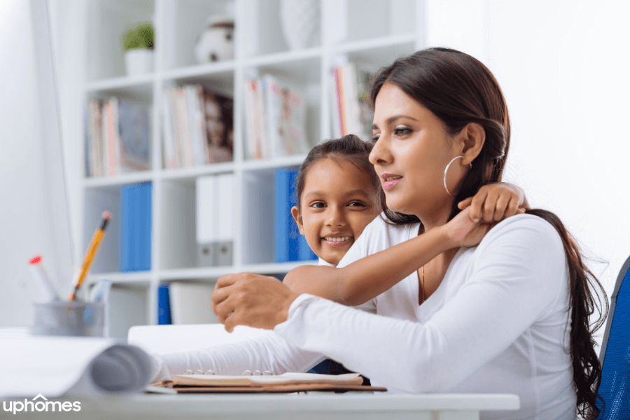 Single Mom working on the computer while daughter wraps her hands around mom giving her a hug and showing mom love and appreciation