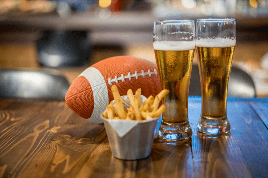 two beers, fries, and a football on a wood table