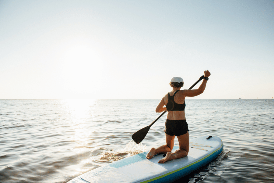 woman paddle-boarding in calm water during sunset