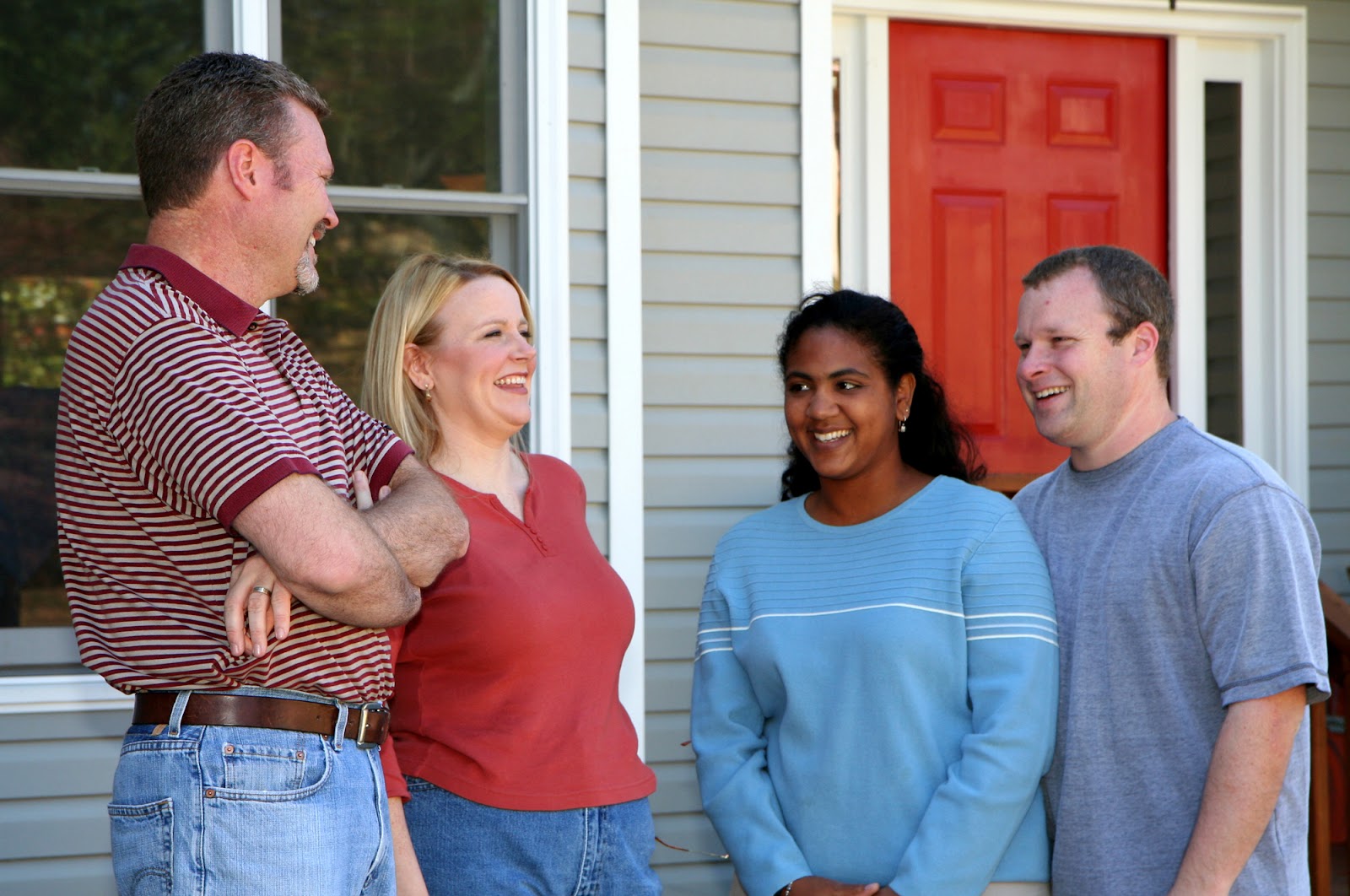 Neighboring couples smile and converse outside a home.
