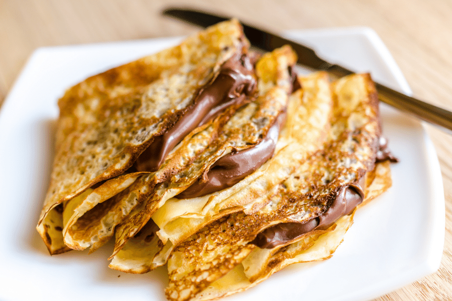 Crepes with Nutella filling on a white plate with knife