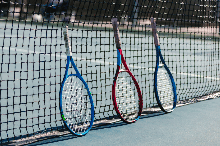 three tennis racquets leaning against a tennis court net