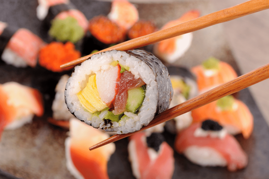 holding a sushi roll with chop sticks