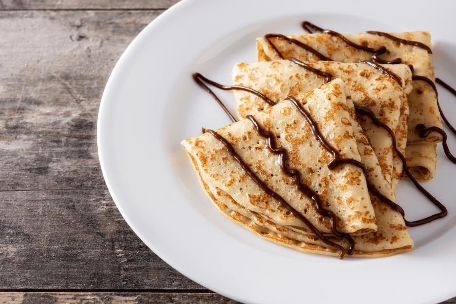 Image of three crepes with chocolate drizzle on a white plate