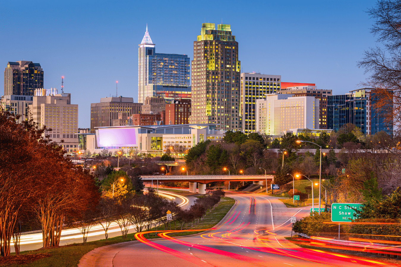 Photo of downtown Raleigh skyline from the interstate leading into the city at night time