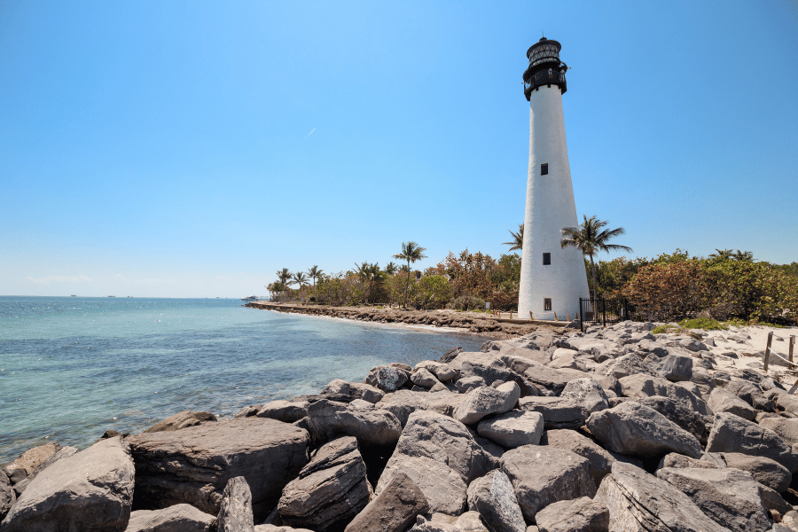 White lighthouse in Key Biscayne, FL near palm trees and rocks