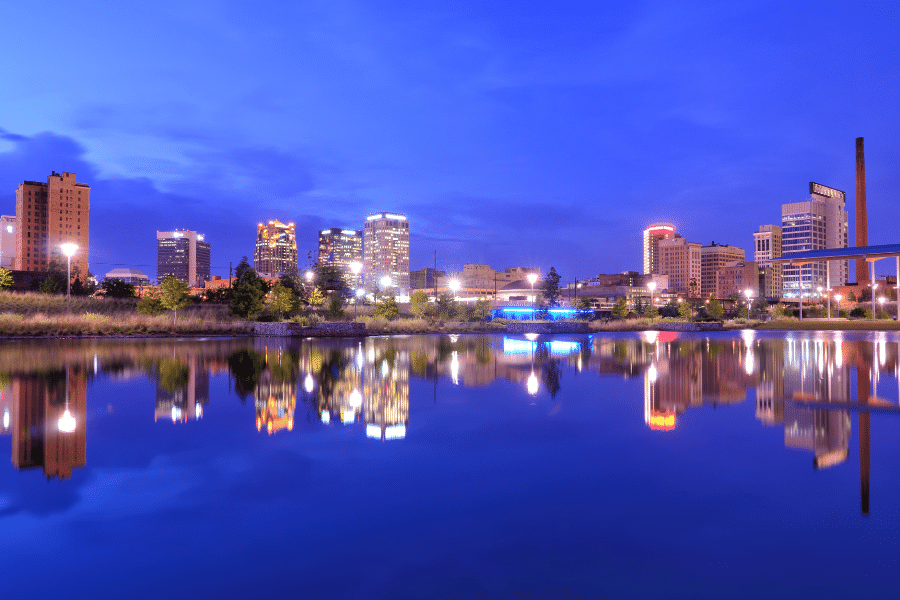 cityscape of Birmingham, AL near the water at night with buildings and bright lights