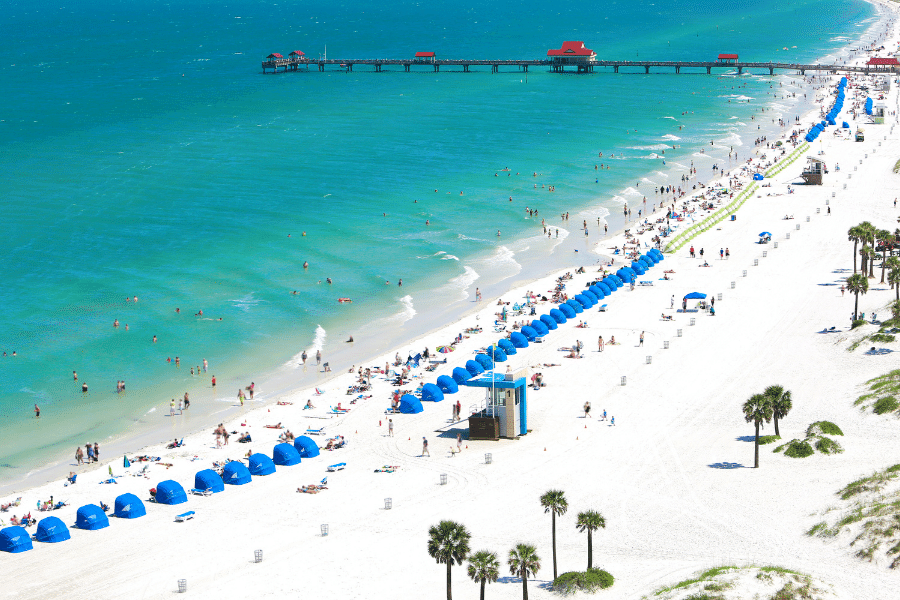 View of Clearwater Beach with palm trees, sand, blue umbrellas, and a pier 