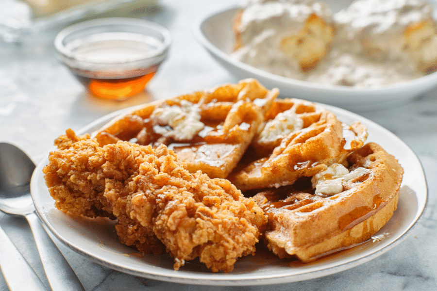 chicken and waffles with a cup of syrup