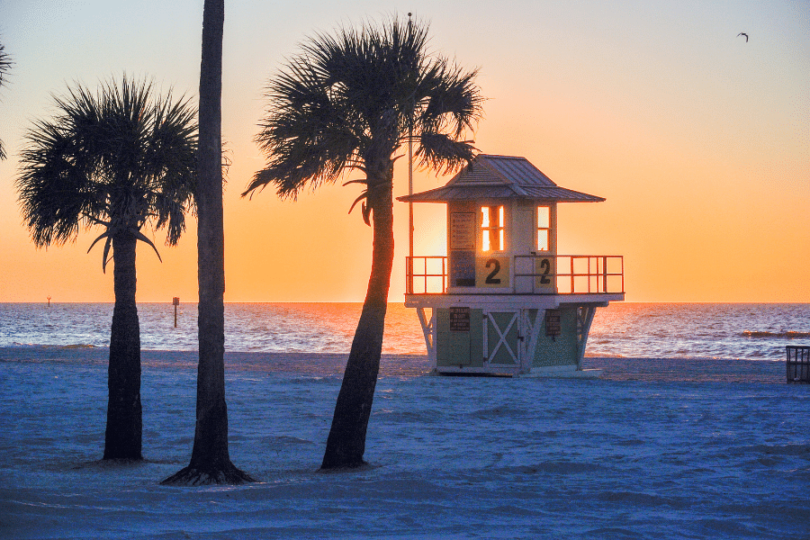 Orange sunset on Clearwater Beach with palm trees and lifeguard stand