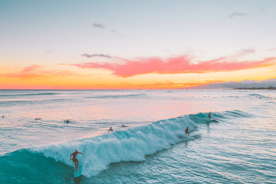 People surfing at orange and pink sunset in Hawaii 