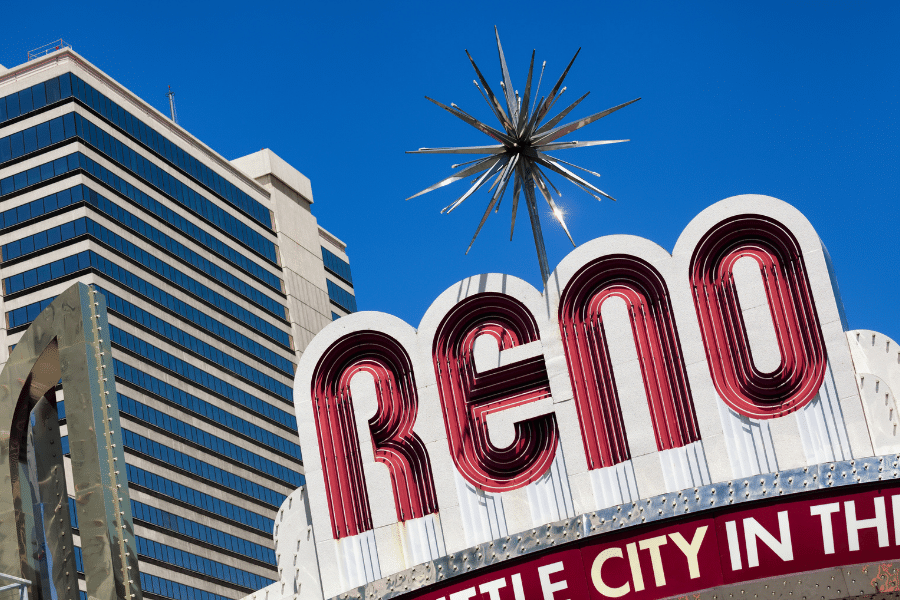 Red and white Reno sign in Reno, NV on a sunny day surrounded by buildings