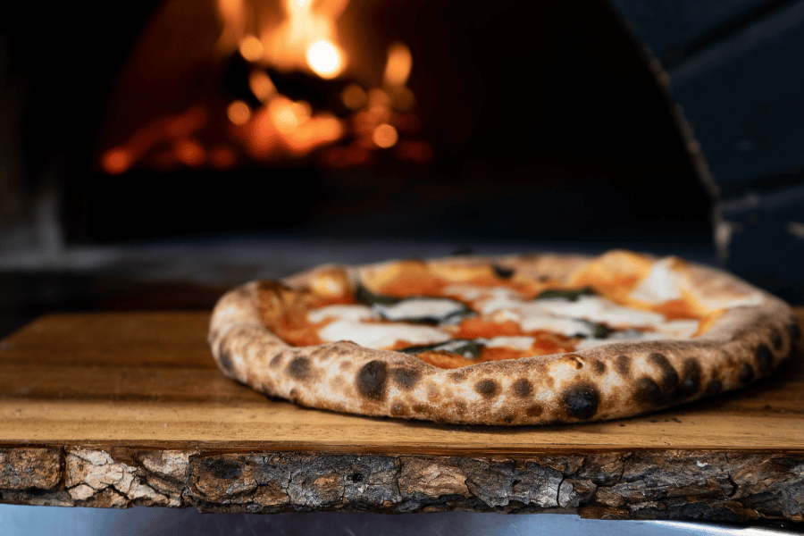 freshly made pizza in front of wood-fire pizza oven 