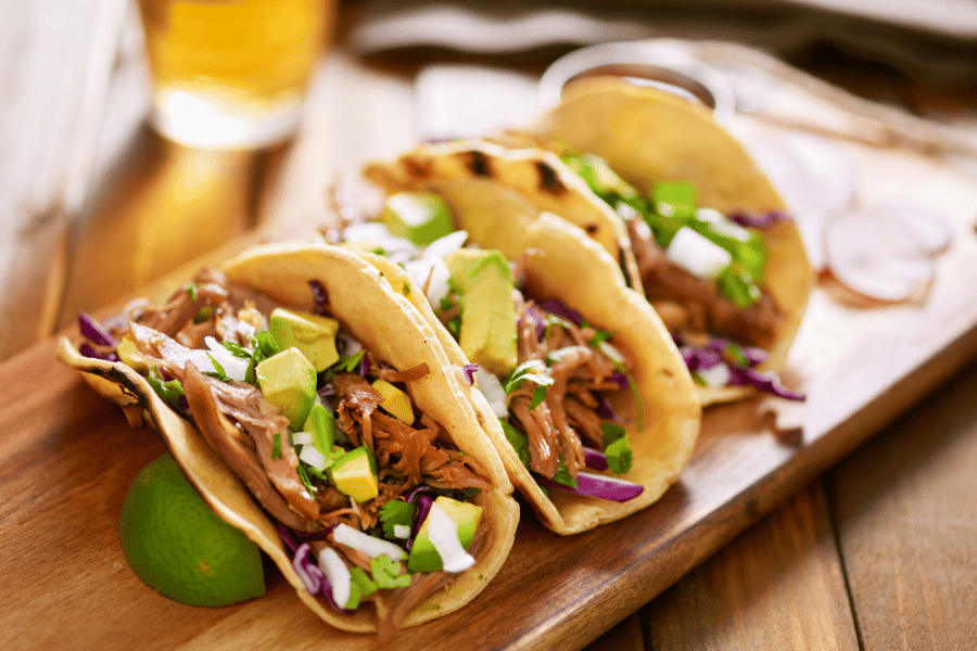 three tacos with lime on a wood board 