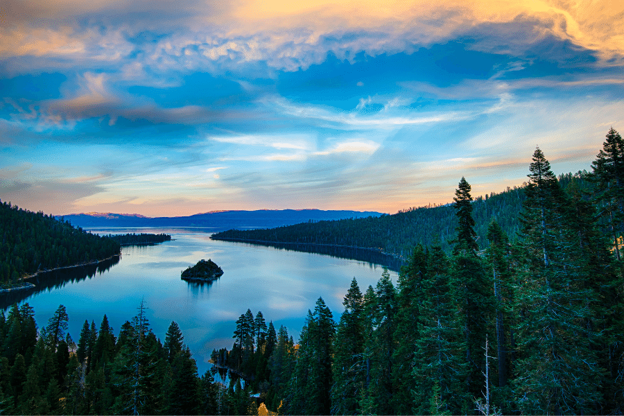 Lake Tahoe during the sunset with still blue water and tons of tall trees 