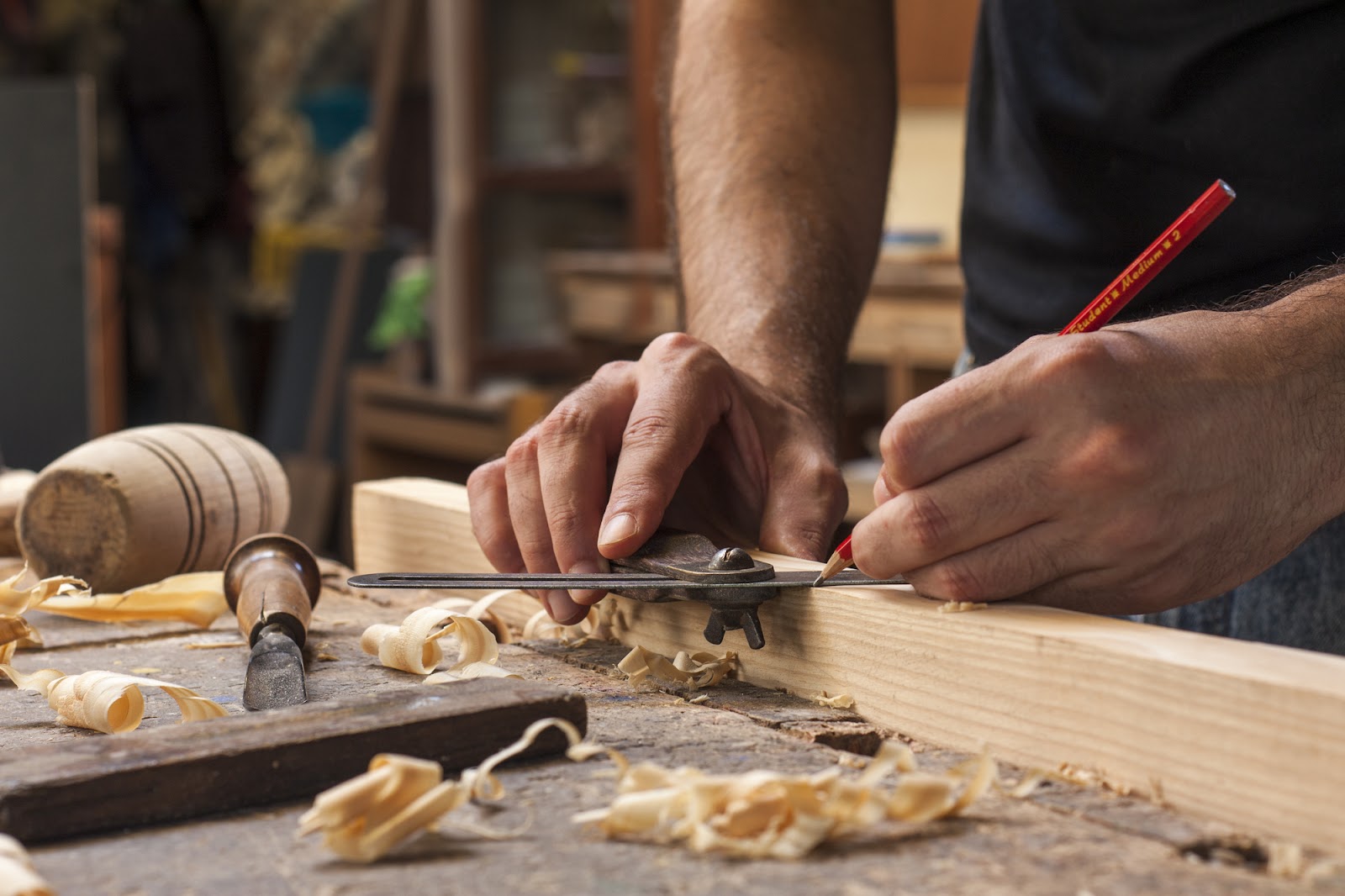 A carpenter making measurements at their woodworking table.