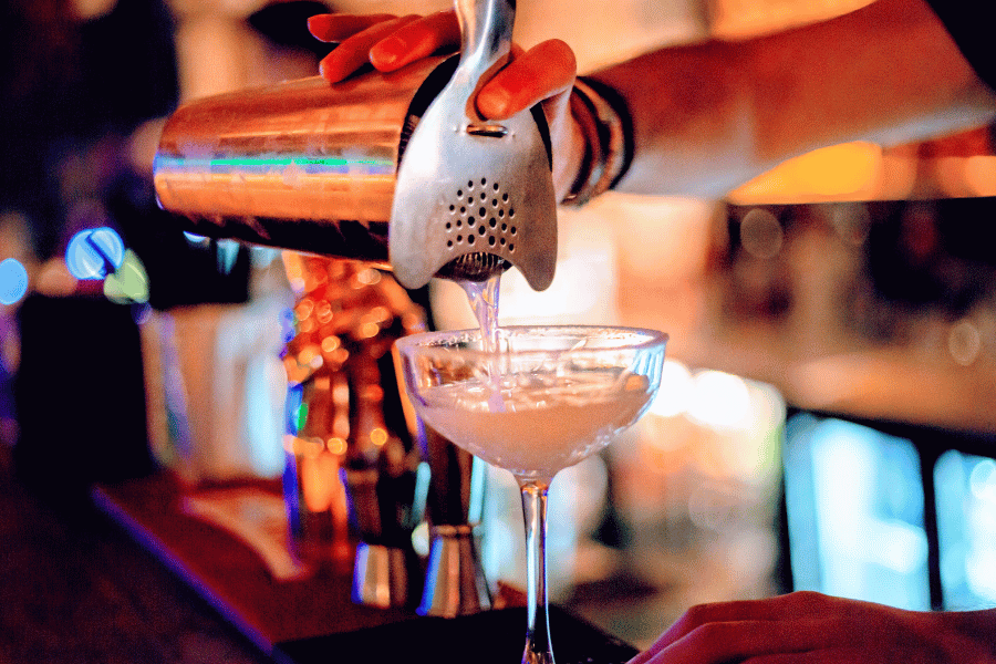 bar tender pouring a cocktail in a glass 