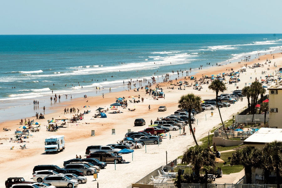 Large crowd at Ormond Beach with cars parked on the beach and palm trees