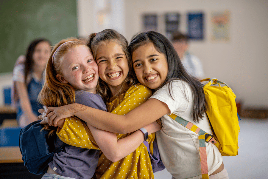 three kids hugging each other in school with backpacks