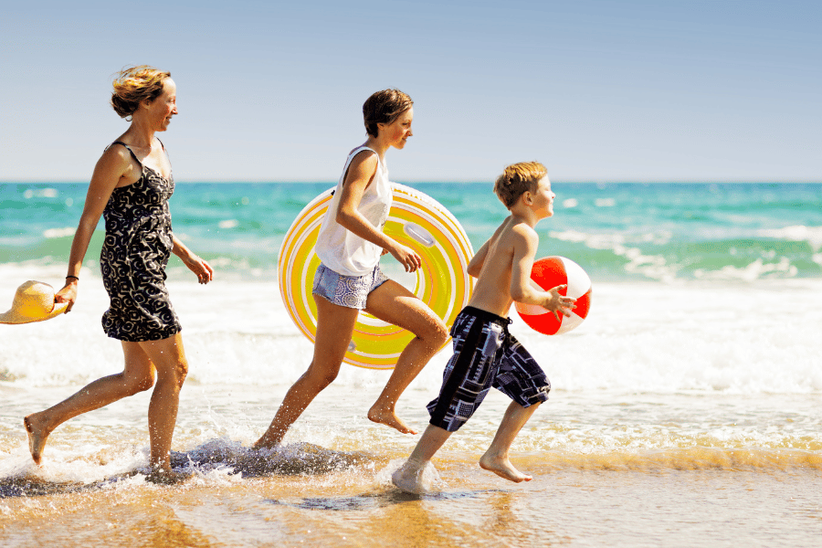 Photo of a family running on the beach with beach toys 