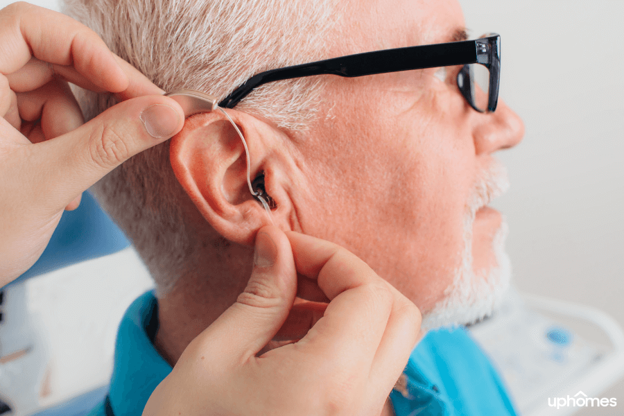 Close up image of a Doctor installing hearing aids on to an older patient who is losing his hearing