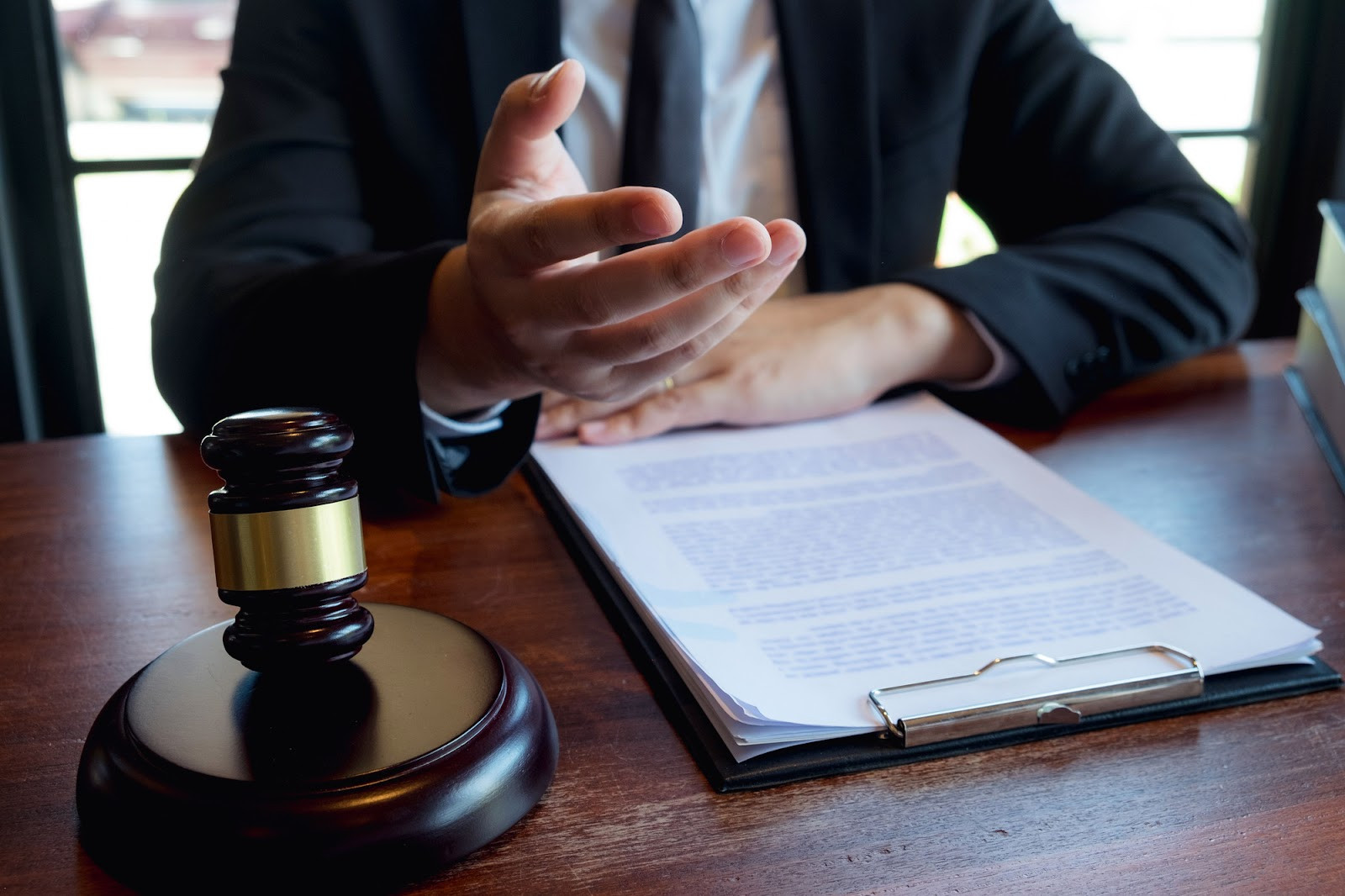 A closeup of a lawyer giving advice, sitting at their desk behind a gavel and clipboard full of legal papers. 