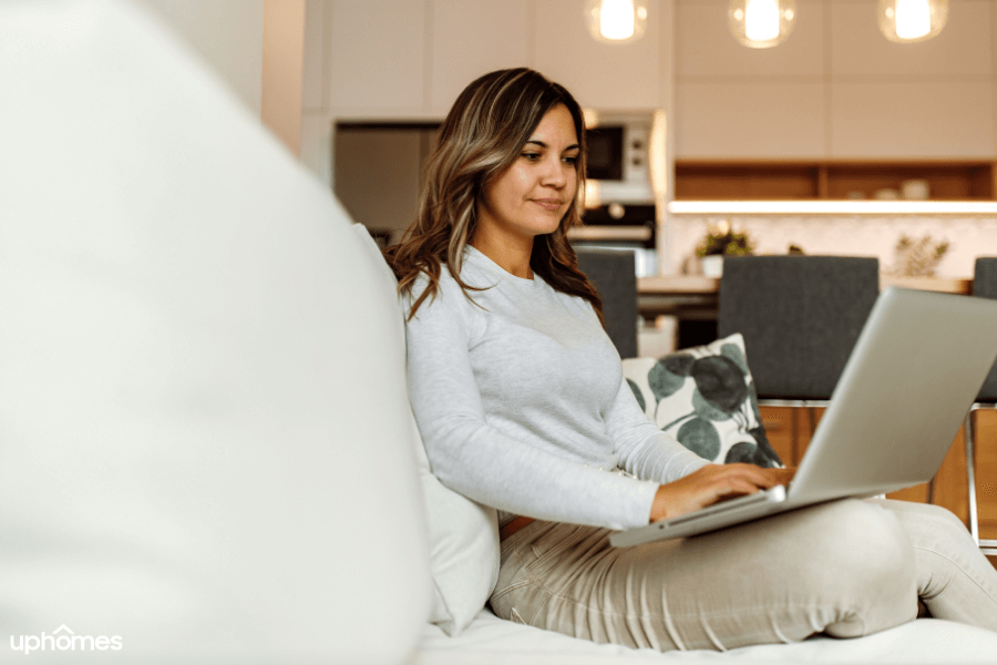 A woman who is living alone sitting on the couch working on her laptop