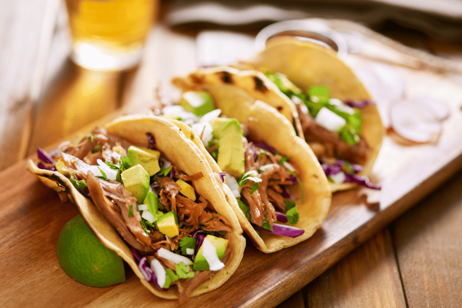delicious-tacos.png three tacos with lime on a wood board
